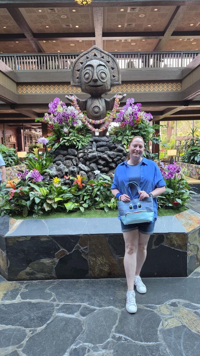 Kelly in a Stitch bound standing in front of the statue in the lobby of Disney’s Polynesian Village Resort