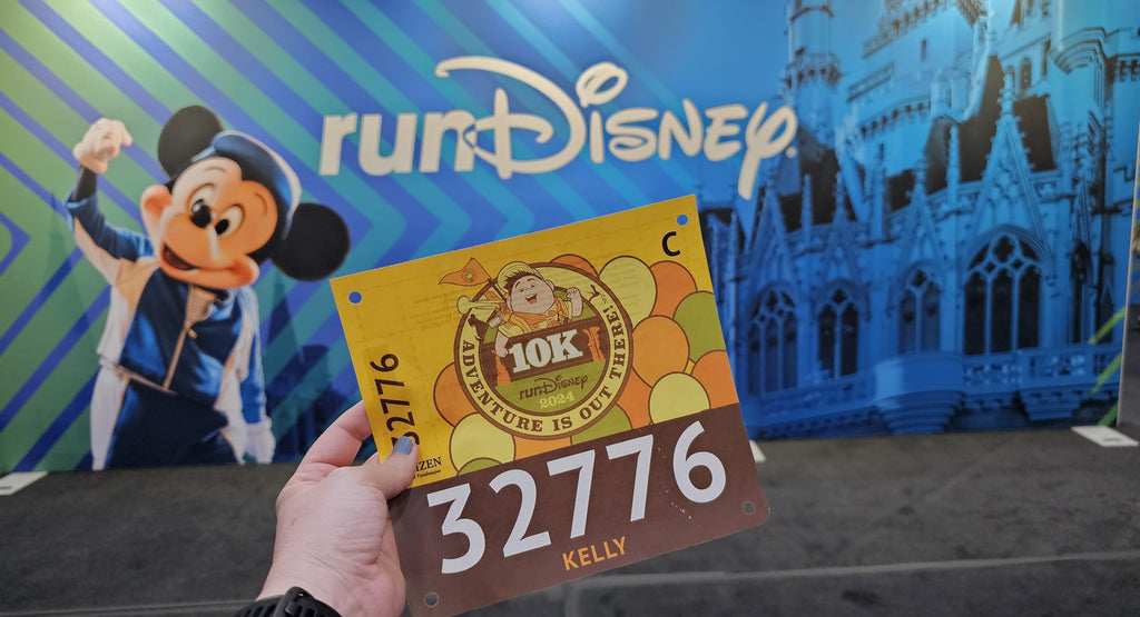 Springtime Surprise 10K race bib with a RunDisney sign featuring Mickey Mouse in the background