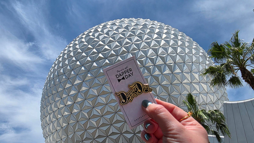 Dapper Day pin being held up in from of the geosphere at Epcot