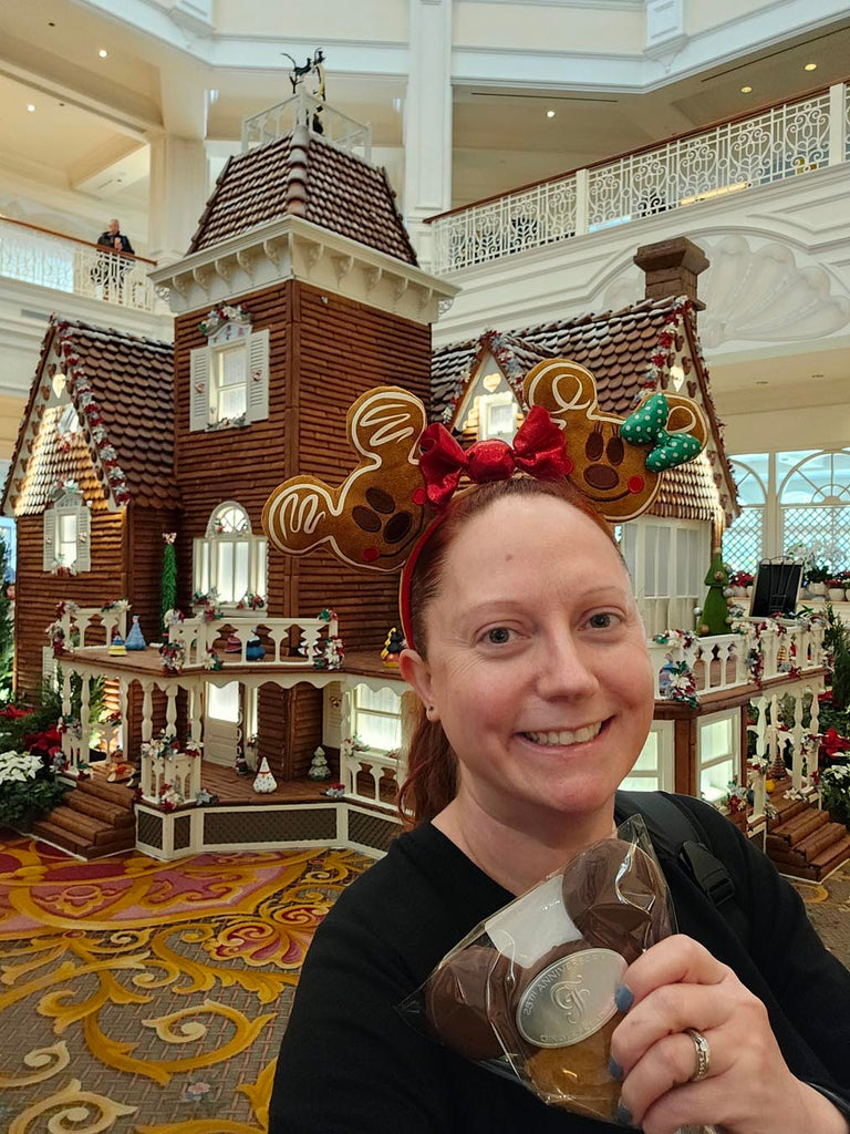 Kelly holding a gingerbread cookie in front of a gingerbread house at Disney’s Grand Floridian