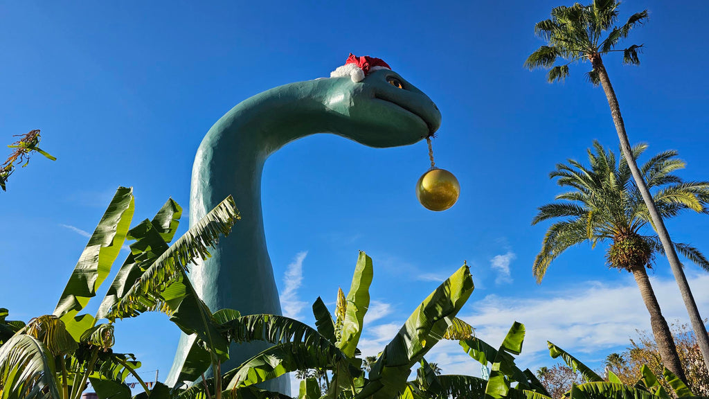 Gertie the Dinosaur wearing a Santa Hat and a Christmas ornament hanging out of her mouth at Disney’s Hollywood Studios