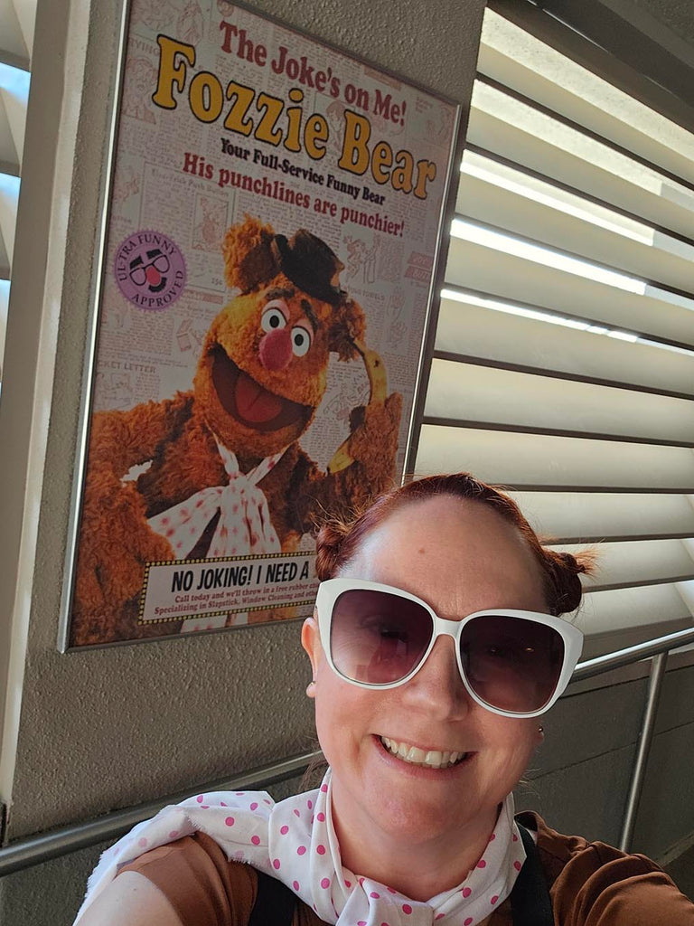 Kelly bounding as Fozzie Bear in front of a poster for Fozzie Bear